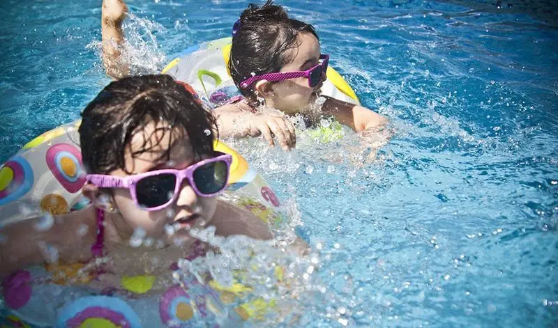  Dos ni&ntilde;os equipados con flotadores y gafas de sol juegan en una piscina. 