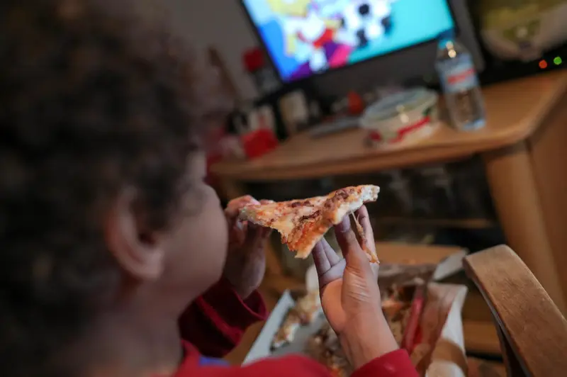  Archivo - Un ni&ntilde;o come un trozo de pizza del men&uacute; infantil de Telepizza mientras ve la televisi&oacute;n en su casa, tras recoger el men&uacute; en un establecimiento de Telepizza. - Jes&uacute;s Hell&iacute;n - Europa Press - Archivo 