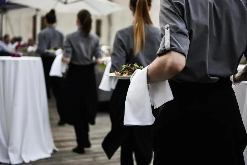 Waiter carrying plates with meat dish on some festive event