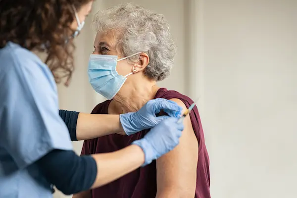 General practitioner vaccinating old patient in private clinic with copy space. Doctor giving injection to senior woman at hospital. Nurse holding syringe and using cotton before make Covid-19 or coronavirus vaccine.