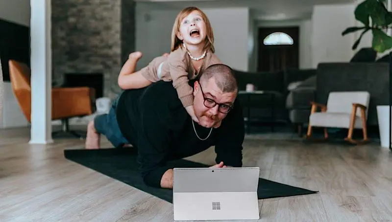 <p> Un padre haciendo ejercicio con su hija mientras trabaja. Fuente: Surface. </p>
