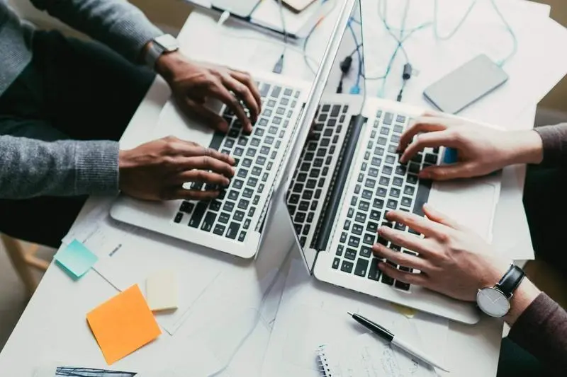  View of an african american and caucasian man collaborating on two laptops 