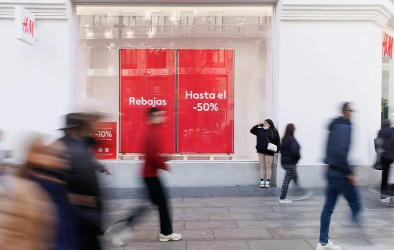  Varias personas caminan frente a una tienda de H&M con el cartel de rebajas 