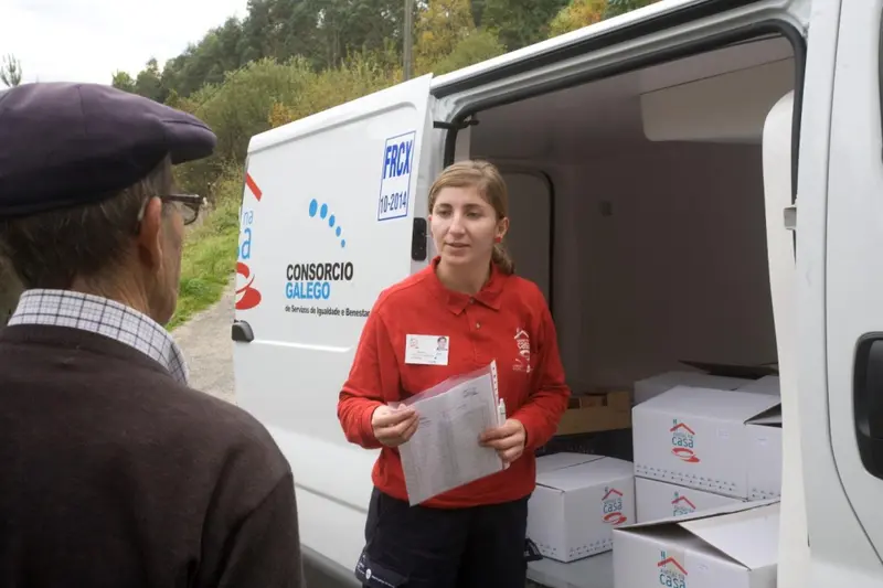  Ayudante de "Xantar na casa" con una persona mayor - Foto recogida de la p&aacute;gina web de la Xunta de Galicia 