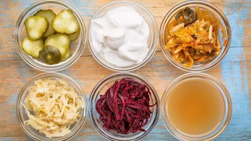 a set of fermented food great for gut health - top view of glass bowls against grunge wood:  cucumber pickles,  coconut milk yogurt, kimchi, sauerkraut, red beets, apple cider vinegar 