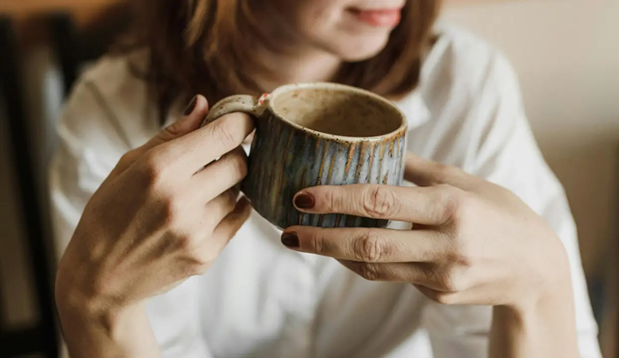  Una mujer sostiene una taza entre su manos. 