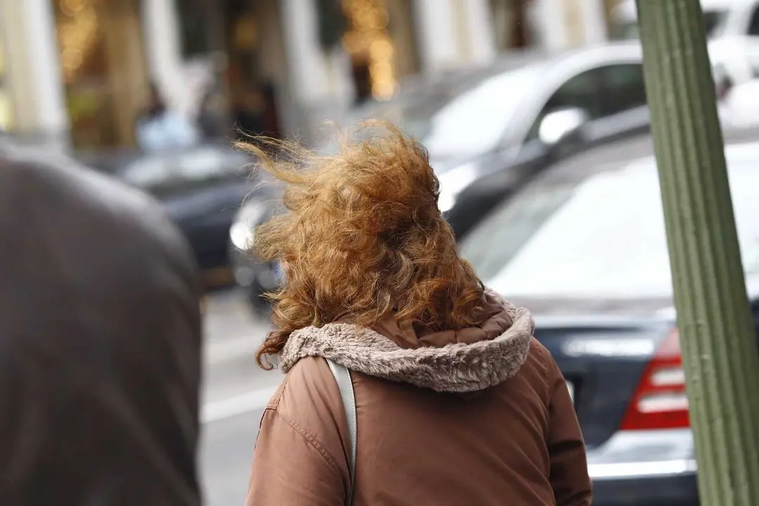 Archivo - Una mujer camina por la calle en un d&iacute;a de viento. Imagen de archivo