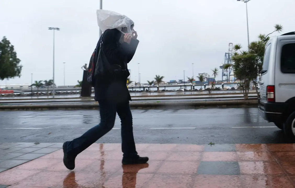 Archivo - Una persona camina con una bolsa en la cabeza por las fuertes lluvias  