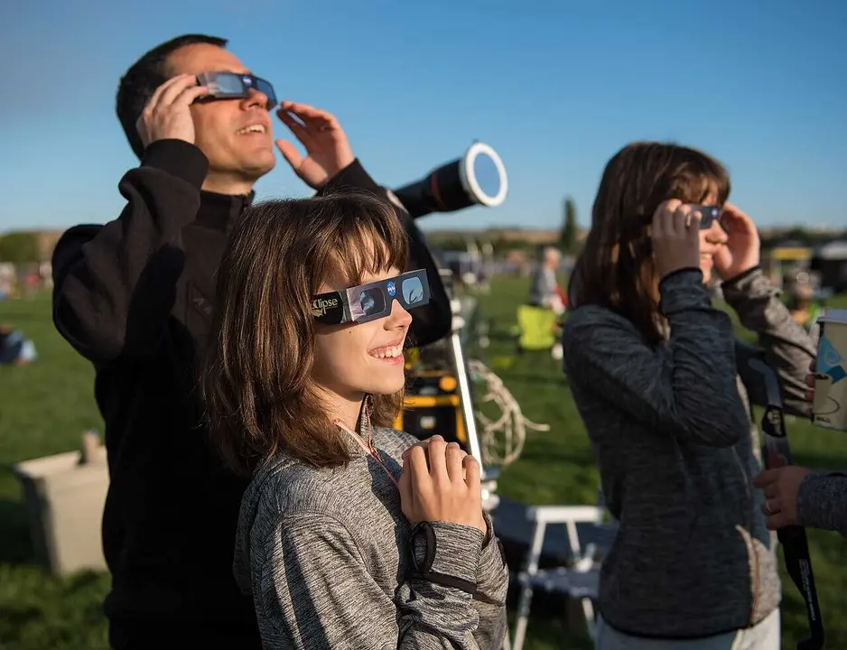 Klaus Koschinsky, left, and his daughters, Claudia, center, and Tanja, right, from Munich, Germany, are seen as they watch a total solar eclipse through protective glasses in Madras, Oregon on Monday, Aug. 21, 2017. A total solar eclipse swept across a narrow portion of the contiguous United States from Lincoln Beach, Oregon to Charleston, South Carolina. A partial solar eclipse was visible across the entire North American continent along with parts of South America, Africa, and Europe.  Photo Credit: (NASA/Aubrey Gemignani)