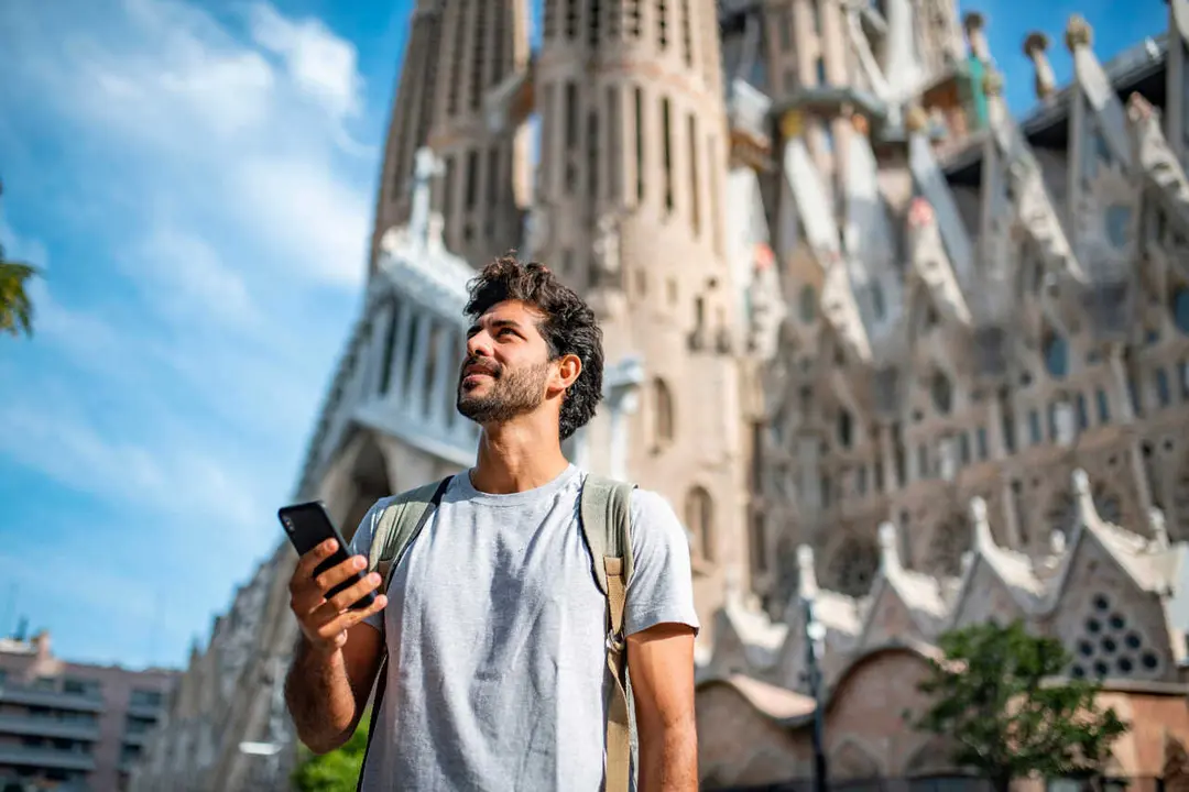 Archivo - Vista de un  turista hispano de 30 a&ntilde;os usando un tel&eacute;fono inteligente como gu&iacute;a tur&iacute;stica, con la Sagrada Familia de fondo
