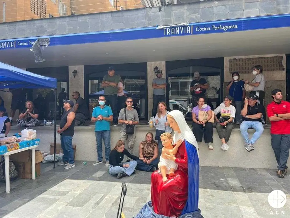 Personas en la calle en Caracas, rezando juntas en torno a una imagen de la Virgen y junto a un puesto de ayuda de la Iglesia cat&oacute;lica.