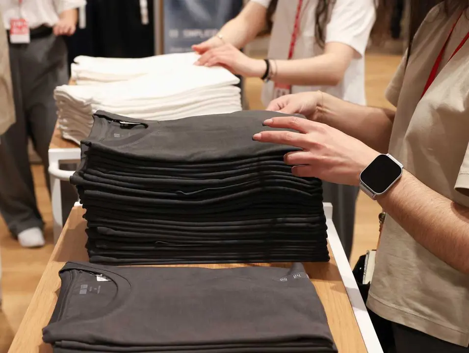 Archivo - Varios dependientes colocan ropa en una tienda de moda 