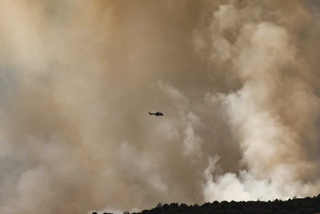 Helic&oacute;ptero vuela entre humo del fuego forestal, a 25 de julio de 2026, en Navaluenga, &Aacute;vila, Castilla y Le&oacute;n (Espa&ntilde;a). El incendio forestal de Burgohondo (&Aacute;vila), que afronta este s&aacute;bado su cuarta jornada, ha obligado a ordenar la evacuaci&oacute;n preventiva d