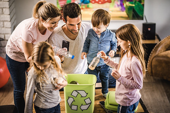 Young happy parents and their kids putting garbage into recycle bin at home.