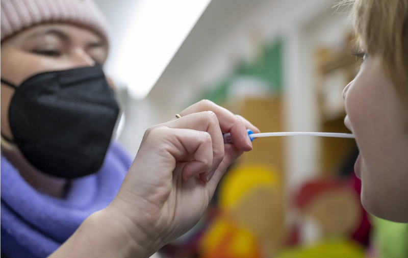 <p> 10 January 2022, Bavaria, Munich: A woman takes a Lollitest swab from a child at the entrance to the Montessori Center daycare center. - Peter Kneffel/dpa </p>