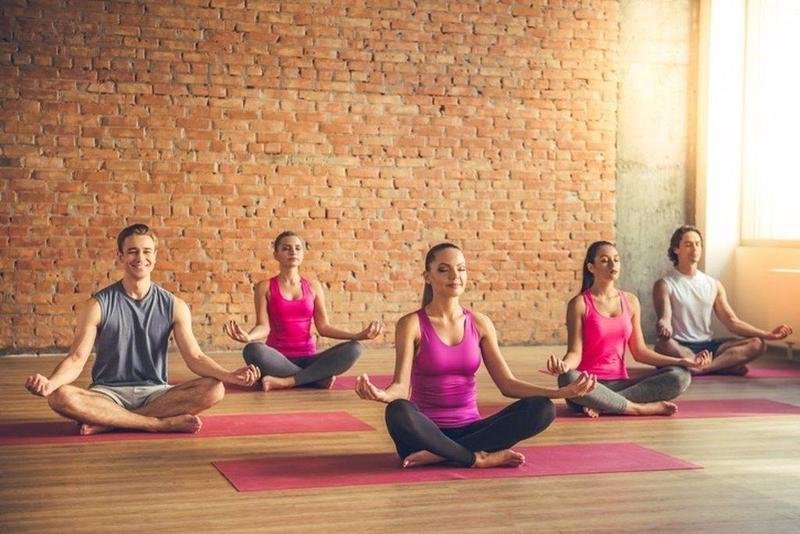 Beautiful sports people are sitting in lotus position and smiling while doing yoga in modern fitness hall