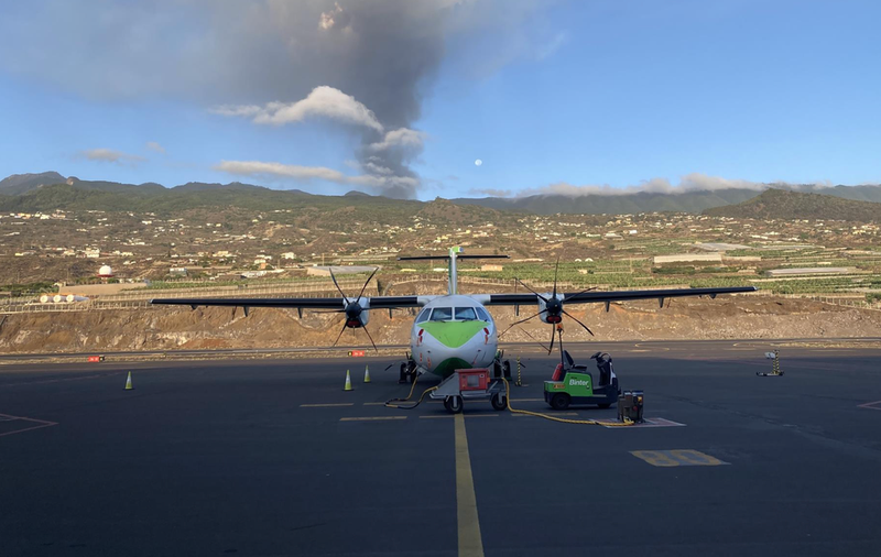 <p> Un avión de Binter en la pista del aeropuerto de La Palma, con el volcán en erupción al fondo - BINTER </p>