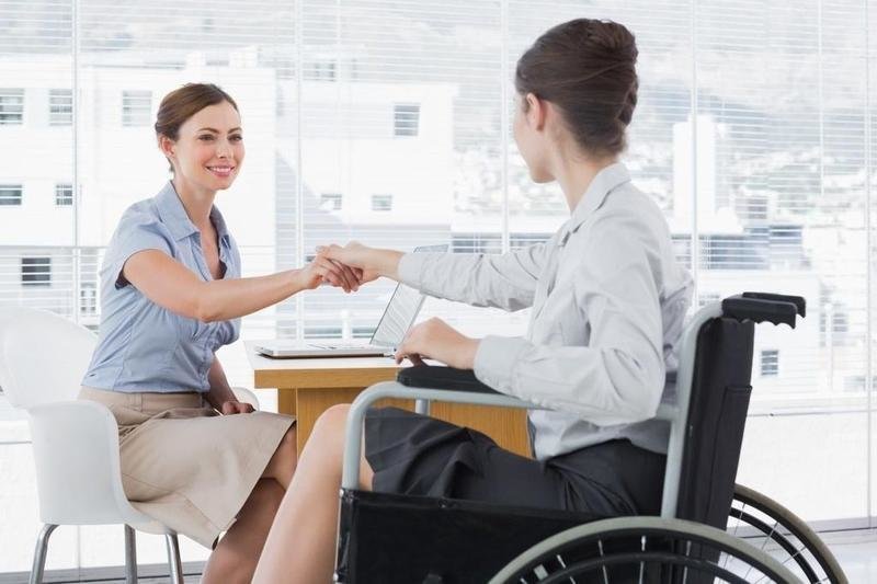 Businesswoman shaking hands with disabled colleague at desk in office