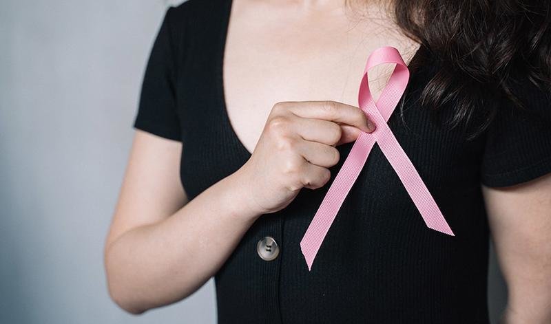 <p> Una mujer se coloca el lazo rosa en solidaridad con las afectadas por cáncer de mama. </p>