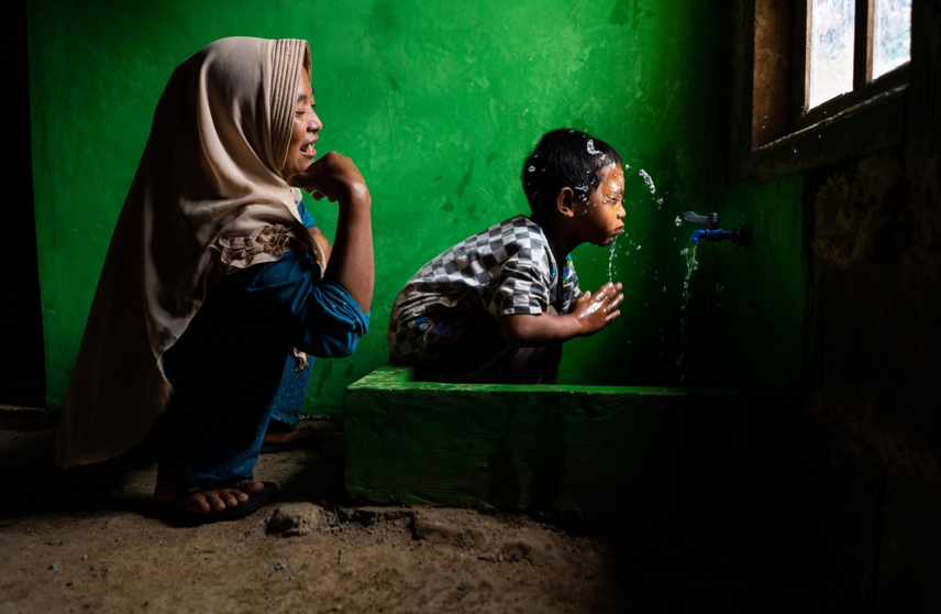  Archivo - Wahyu observa a su hijo Rizki, de 4 años, lavándose la cara en una nueva instalación de agua potable en su casa, en Tlogopakis, Indonesia. - UNICEF/IJAZAH - Archivo 