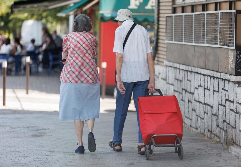  Una pareja de mayores caminan con un carro de la compra 