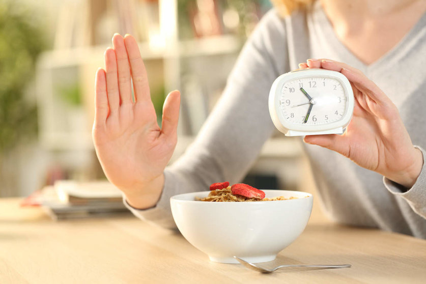  Close up of woman hands on intermittent fasting doing stop sign waiting before eating cereal bowl on a table at home 