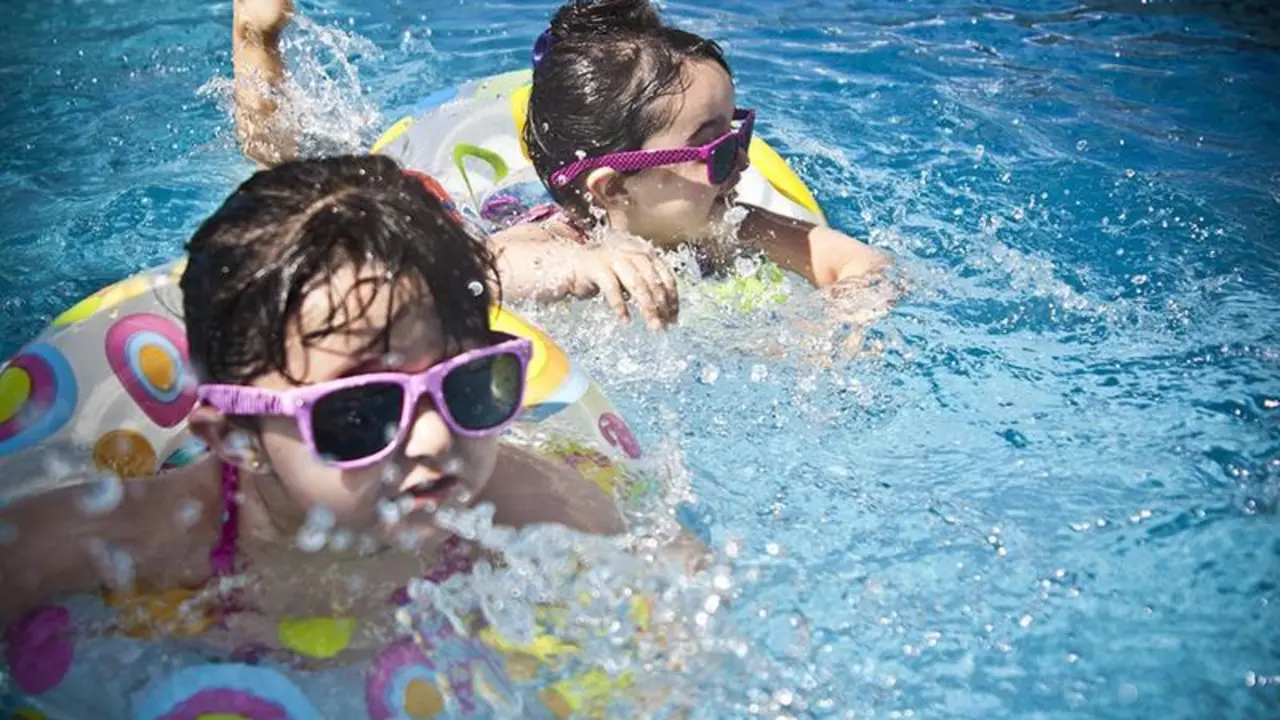  Dos ni&ntilde;os equipados con flotadores y gafas de sol juegan en una piscina. 