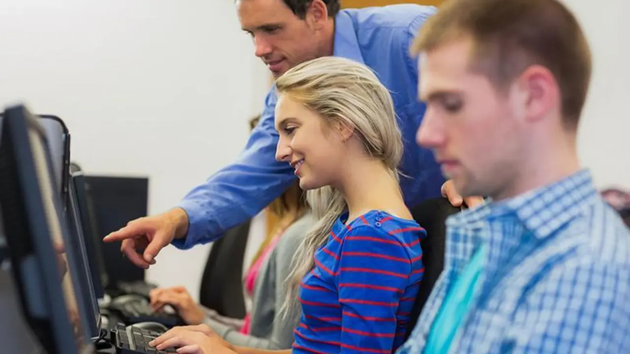Side view of teacher showing something on screen to student in the computer room