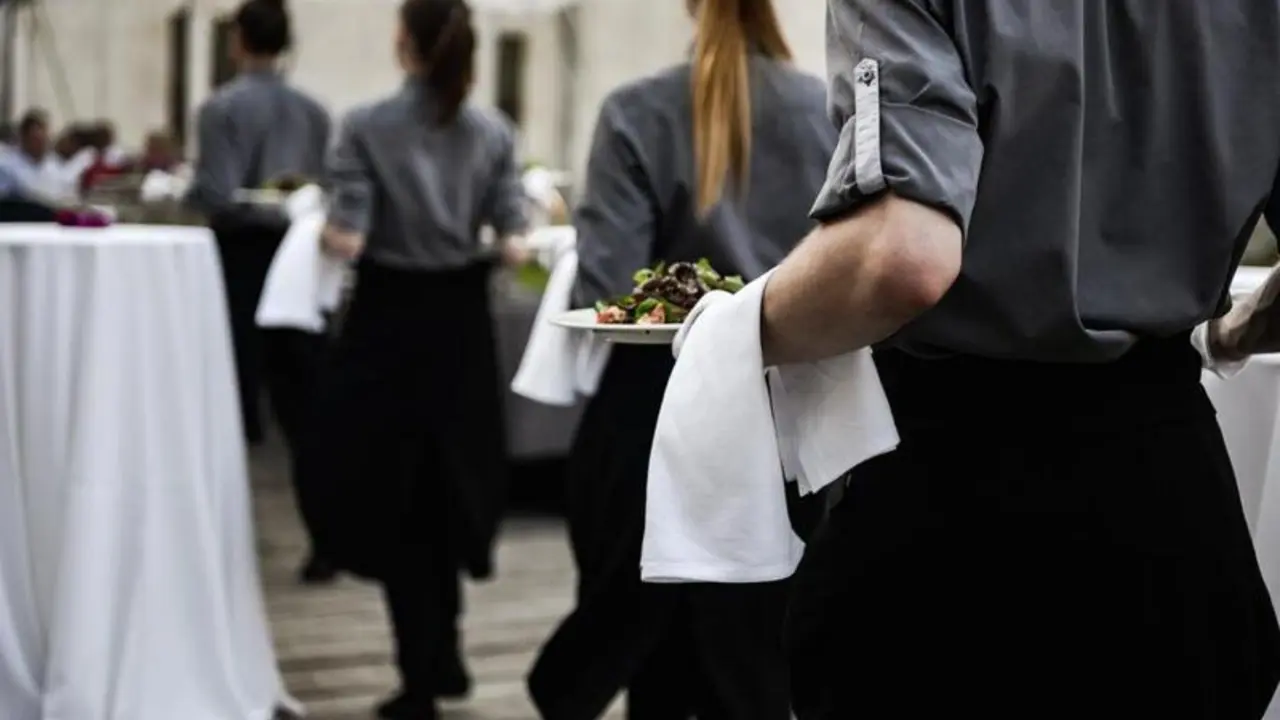 Waiter carrying plates with meat dish on some festive event