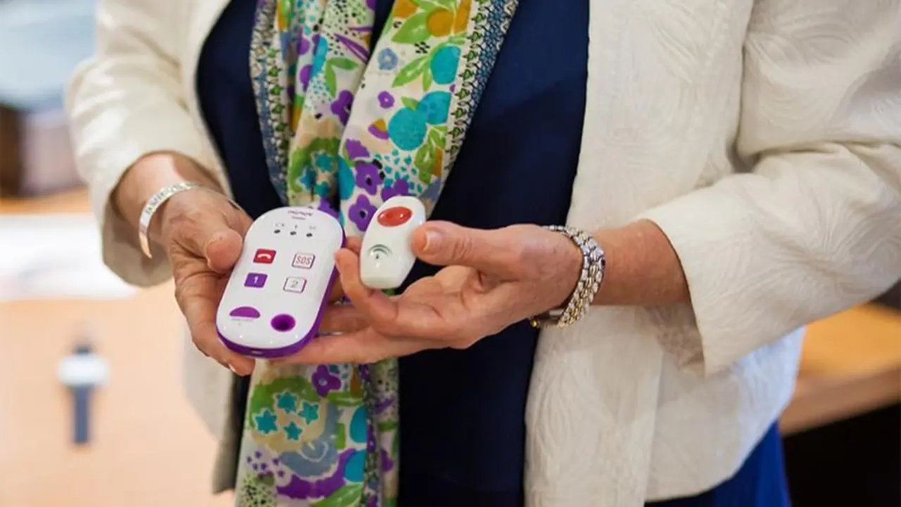 <p> Una mujer sostiene en sus manos dos dispositivos para que los usuarios reclamen ayuda del Servicio de Teleasistencia. </p>