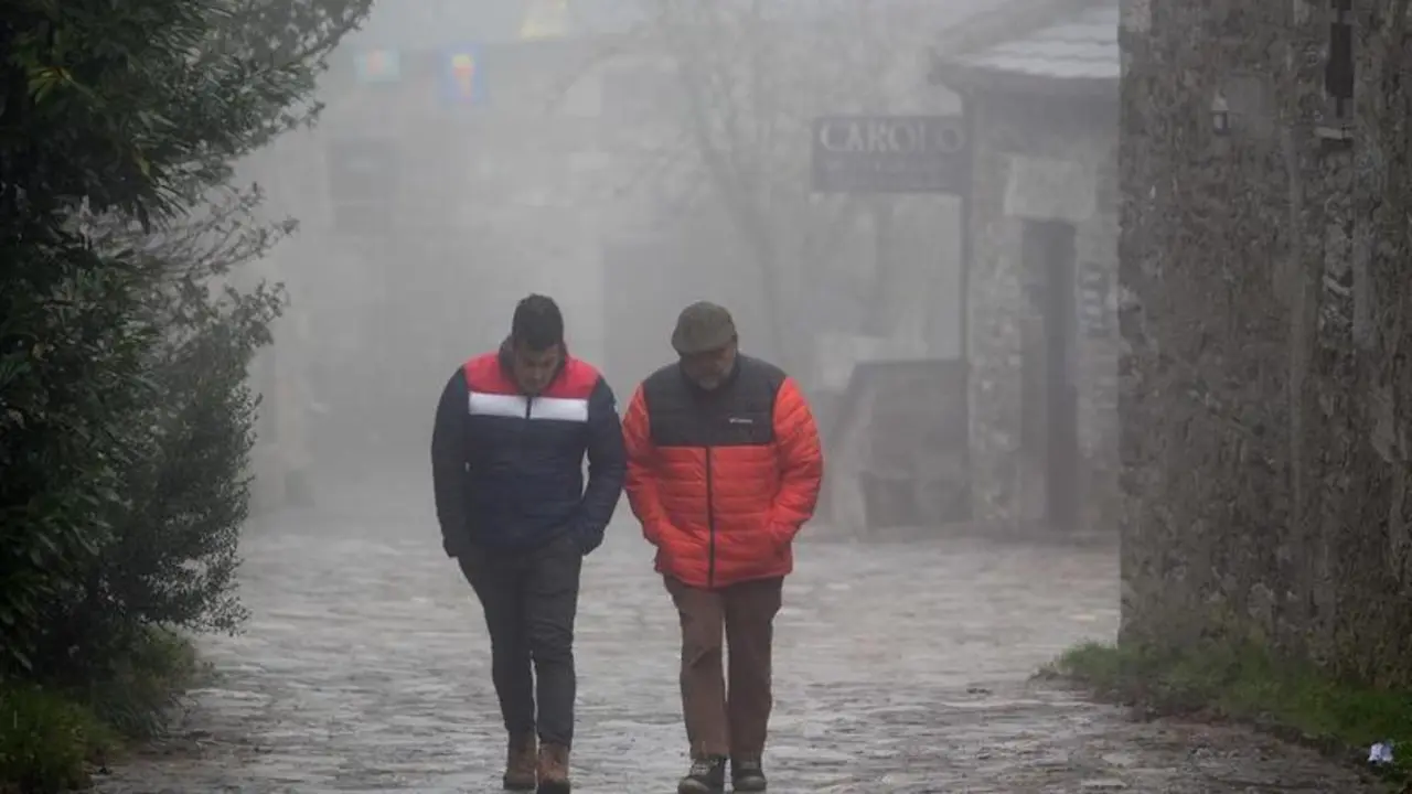 <p> Dos hombres caminando entre la niebla en la aldea prerromana de O Cebreiro </p>