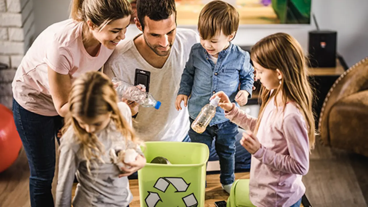 Young happy parents and their kids putting garbage into recycle bin at home.