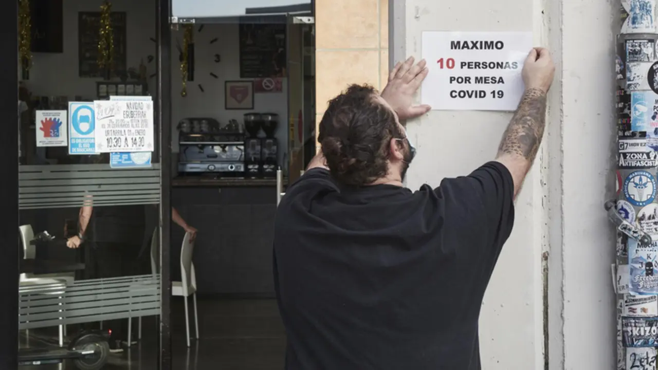 <p> Un camarero coloca un cartel de reducci&oacute;n de aforo por Covid en su local - Eduardo Sanz - Europa Press </p>