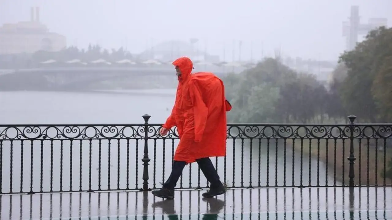 <p> Una persona cruza un puente en Sevilla bajo la lluvia </p>