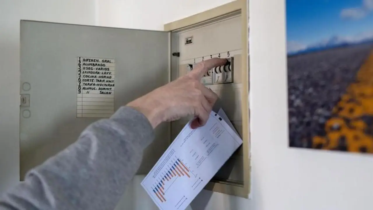 <p> Un hombre sube los plomos de la luz con una factura de luz en la mano </p>