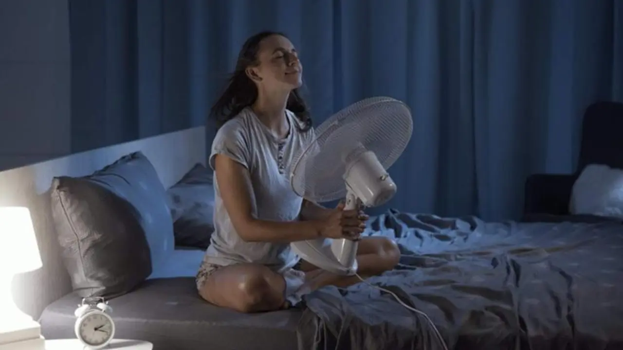 <p> Woman in her bedroom on a hot summer night, she is enjoying fresh air in front of a fan </p>