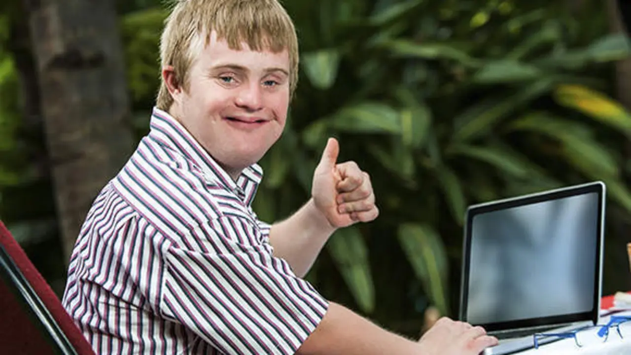 Portrait of handicapped student doing thumbs up sign next to laptop outdoors.