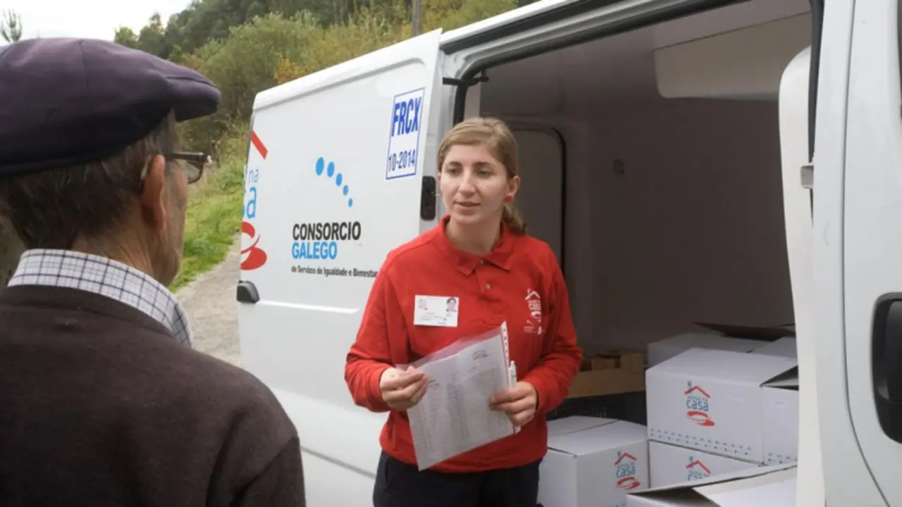  Ayudante de "Xantar na casa" con una persona mayor - Foto recogida de la p&aacute;gina web de la Xunta de Galicia 