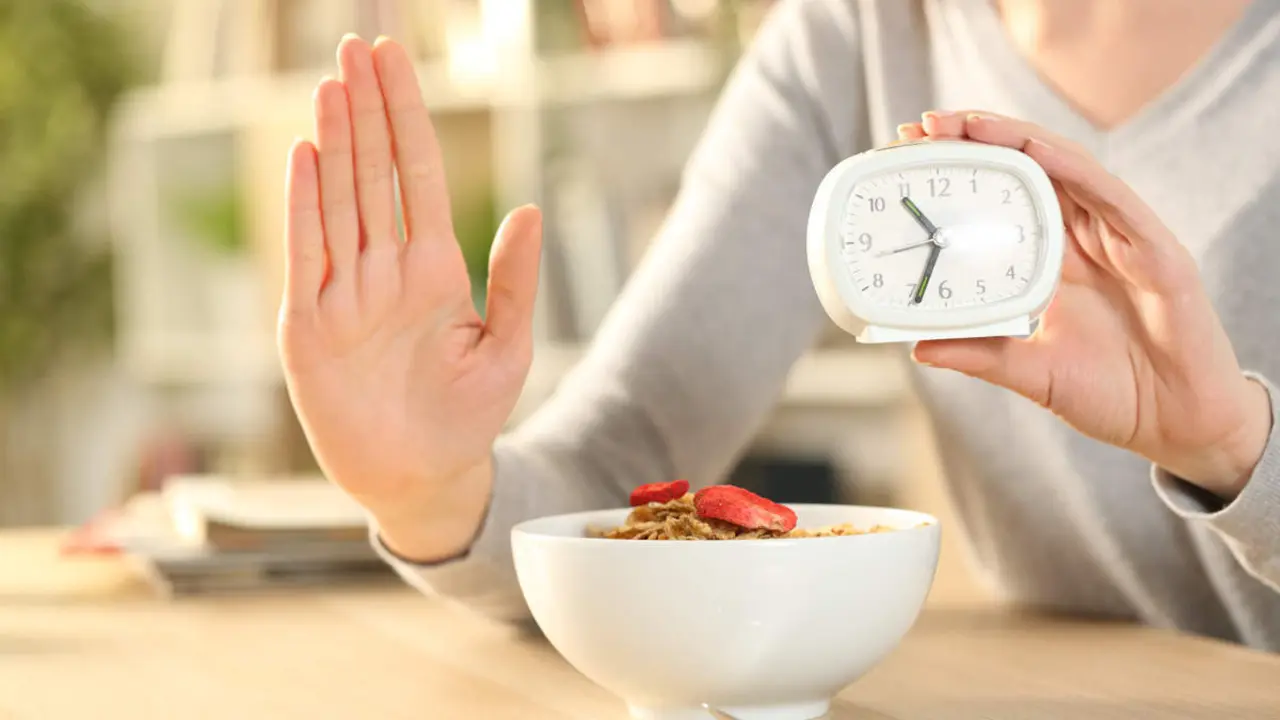  Close up of woman hands on intermittent fasting doing stop sign waiting before eating cereal bowl on a table at home 