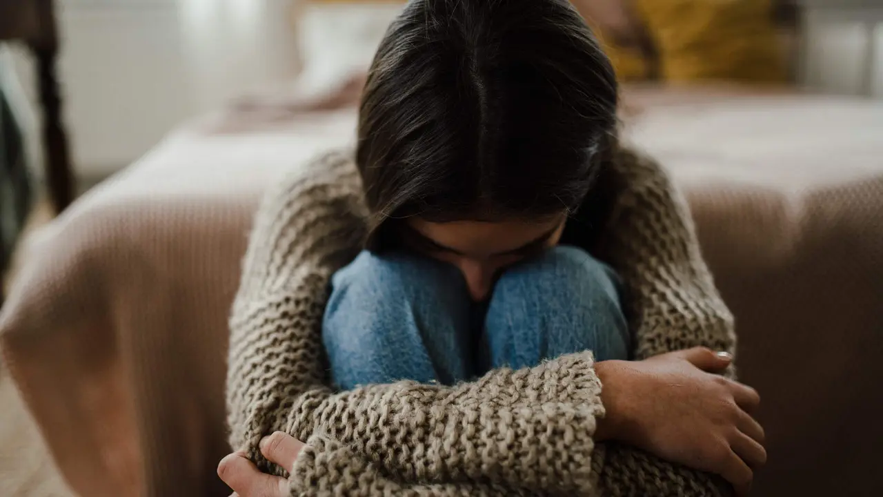  Teenage girl sitting on the floor with head on her knees, koncept of mental health. 
