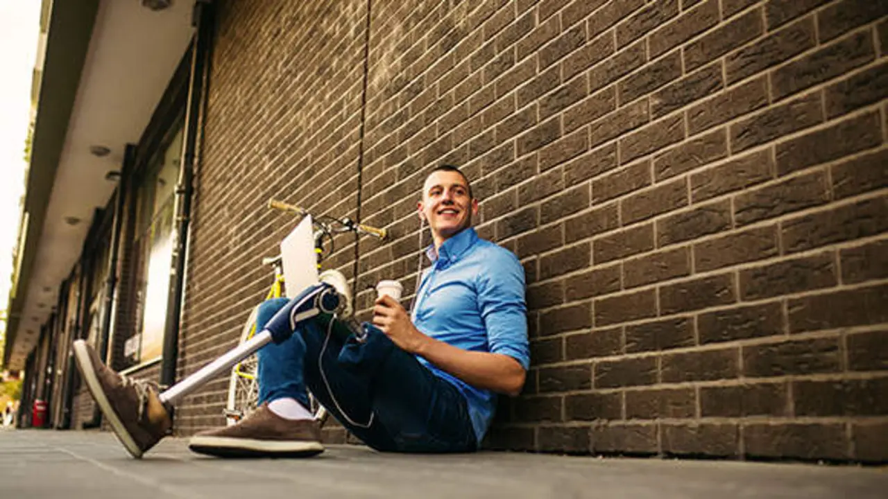 Young male with amputee left leg sitting outdoor on the ground and working on a laptop computer