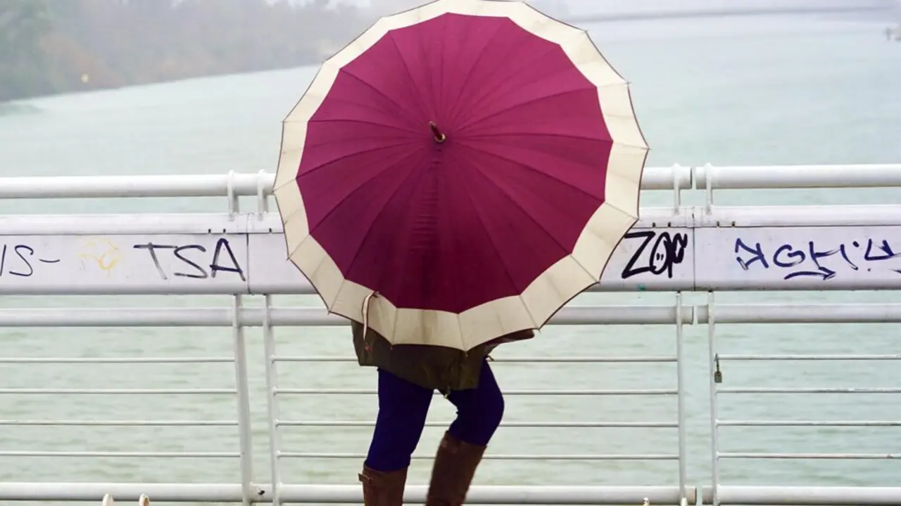  Archivo - Un persona se protege de la lluvia y el viento caminando por la pasarela peatonal de la Cartuja en un d&iacute;a lluvioso y con fuertes rachas de viento en la provincia. En Sevilla (Andaluc&iacute;a, Espa&ntilde;a), a 09 de febrero de 2021. - Eduardo Briones - Europa Press - Archivo 