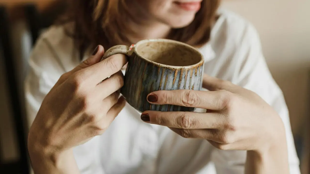  Una mujer sostiene una taza entre su manos. 