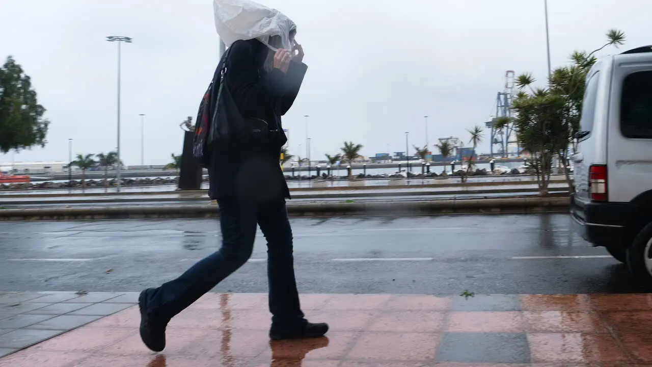 Archivo - Una persona camina con una bolsa en la cabeza por las fuertes lluvias  