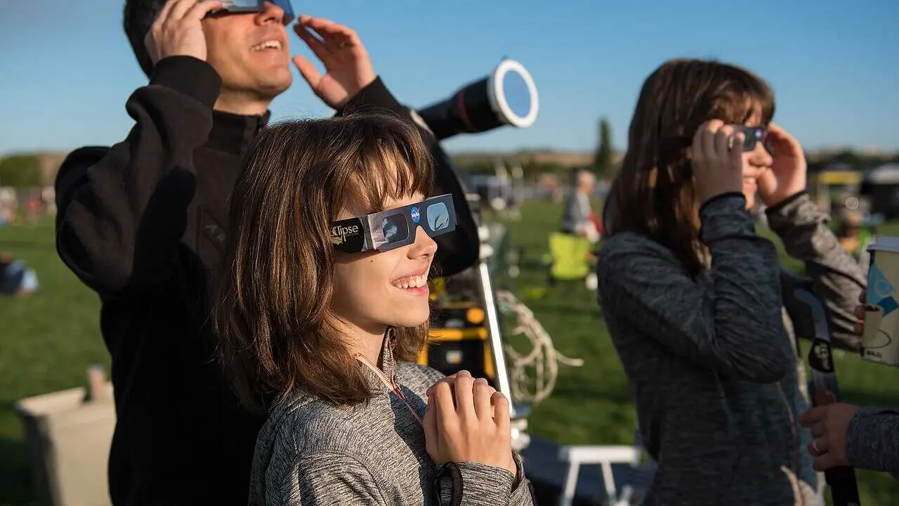 Klaus Koschinsky, left, and his daughters, Claudia, center, and Tanja, right, from Munich, Germany, are seen as they watch a total solar eclipse through protective glasses in Madras, Oregon on Monday, Aug. 21, 2017. A total solar eclipse swept across a narrow portion of the contiguous United States from Lincoln Beach, Oregon to Charleston, South Carolina. A partial solar eclipse was visible across the entire North American continent along with parts of South America, Africa, and Europe.  Photo Credit: (NASA/Aubrey Gemignani)