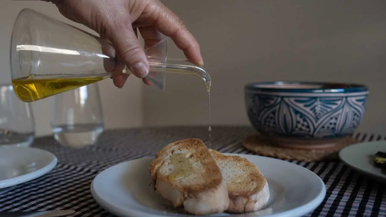 Archivo - Una persona echa aceite de una aceitera a una tostada