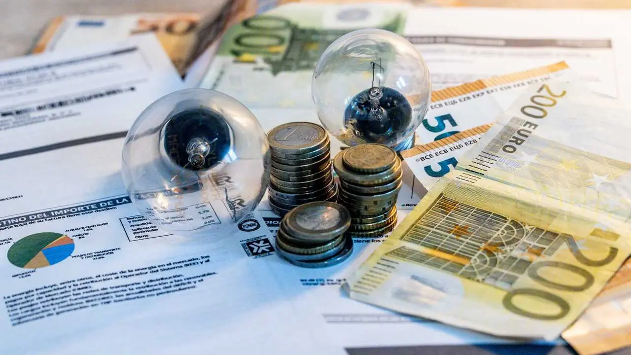 Archivo - Dos bombillas sobre billetes, monedas y facturas en imagen de archivo.