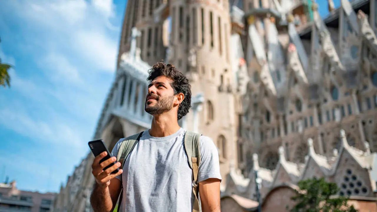 Archivo - Vista de un  turista hispano de 30 a&ntilde;os usando un tel&eacute;fono inteligente como gu&iacute;a tur&iacute;stica, con la Sagrada Familia de fondo