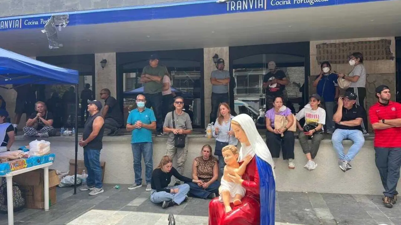 Personas en la calle en Caracas, rezando juntas en torno a una imagen de la Virgen y junto a un puesto de ayuda de la Iglesia cat&oacute;lica.