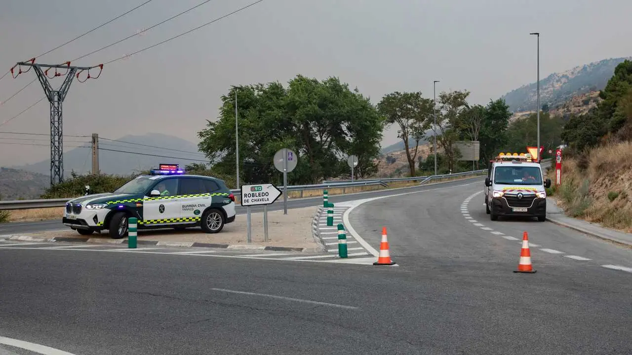 Veh&iacute;culos de la guardia civil vigilan la carretera cortada durante las labores de extinci&oacute;n del incendio forestal